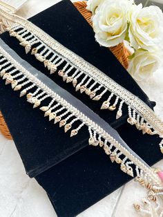 two pieces of jewelry sitting on top of a black velvet bag next to white flowers