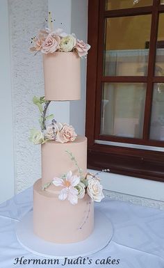 a three tiered cake with flowers on it sitting on top of a table next to a window