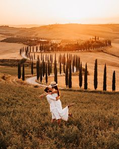 two people holding hands while standing in a field with trees and rolling hills behind them