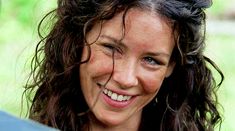 a close up of a woman smiling with wet hair on her head and blue umbrella in the background