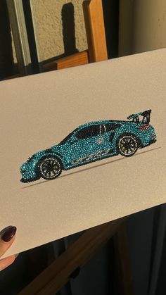 a person holding up a card with a car on it's side and the image is made out of beads