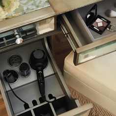 an open drawer with hairdryers and other items in it on a table next to a mirror