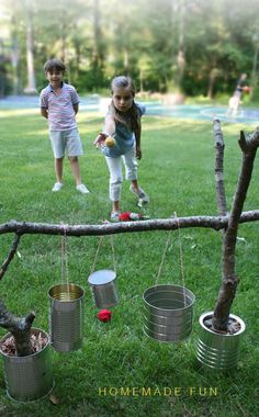 two children playing with tin cans on a tree branch in the grass, and one child is holding an apple