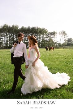 a bride and groom walking through the grass in front of some horses at their wedding