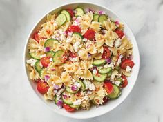 a white bowl filled with pasta salad on top of a marble countertop next to sliced cucumbers