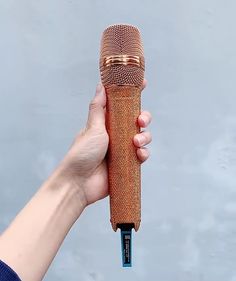 a hand holding an old fashioned microphone in front of a gray background with gold trim