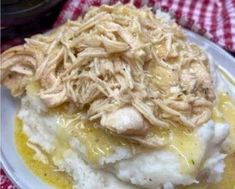 a white plate topped with mashed potatoes covered in chicken and gravy on top of a red checkered table cloth