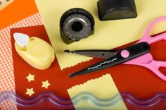 a pair of pink scissors sitting on top of a red and yellow table cloth next to other items