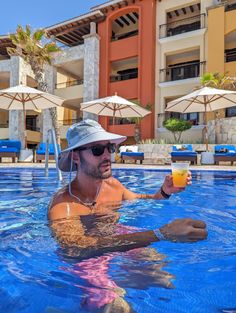 a man sitting in the middle of a swimming pool holding a glass of orange juice