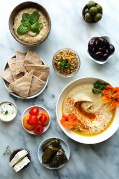 an assortment of food on a table including pita chips, olives and hummus