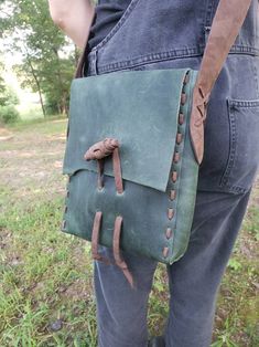 a person holding a green leather bag in their hands and wearing blue jeans with brown straps