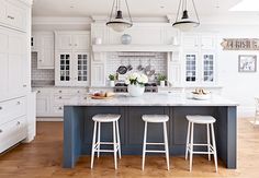 a kitchen with white cabinets and blue island in the center is surrounded by wooden flooring