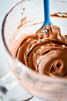 a glass bowl filled with chocolate frosting and a blue plastic spoon sticking out of it