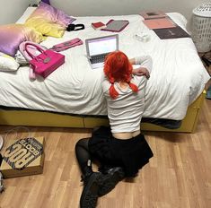 a woman sitting on the floor in front of a bed with her laptop computer open