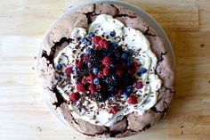 a chocolate cake topped with whipped cream and berries on top of a wooden table next to a fork