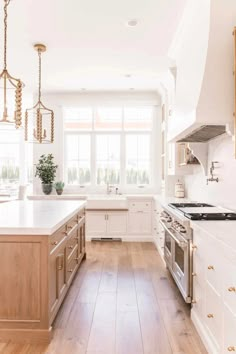 a large kitchen with white cabinets and wood flooring is pictured in this image, there are two chandeliers hanging from the ceiling