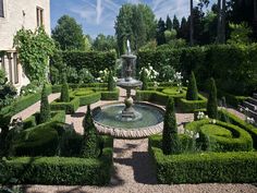 a garden with a fountain surrounded by hedges