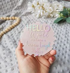 a person holding up a hello world sticker on top of a white bed with flowers