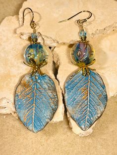 a pair of earrings with blue leaves and glass beads on them sitting on a rock