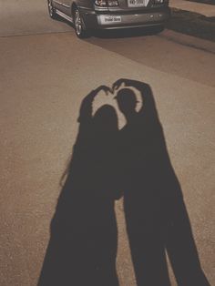 the shadow of two people holding hands in front of a parked car on a street