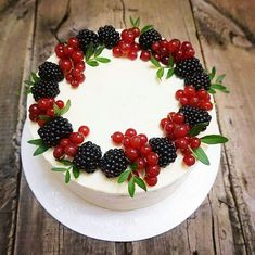 a cake decorated with berries and leaves on a wooden table, ready to be eaten