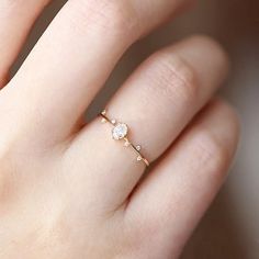 a woman's hand wearing a gold ring with an oval diamond on top and two small diamonds in the middle