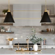 two black lamps hanging over a kitchen island with white counter tops and gold accents on the shelves