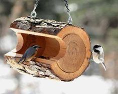 two birds are perched on a bird feeder hanging from chains that have been made to look like wood