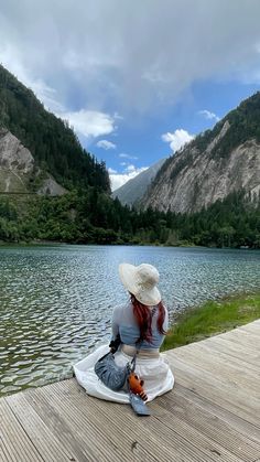 a woman sitting on top of a wooden pier next to a lake