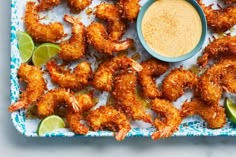 fried shrimp with dipping sauce and limes on a blue platter next to a small bowl