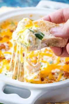 a hand holding a piece of bread over a casserole dish with cheese and spinach