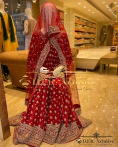 a mannequin dressed in a red bridal gown sits on the floor at a store