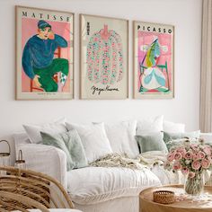 a living room filled with white furniture and paintings on the wall above it's coffee table