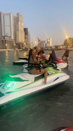 several people riding jet skis in the water with city skyline behind them at dusk