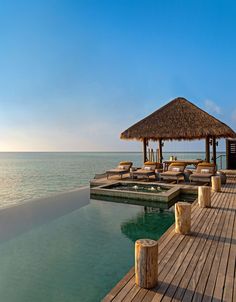 a wooden dock with lounge chairs and thatched roof over the water