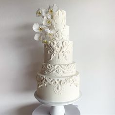 a three tiered white wedding cake with flowers on the top and bottom, sitting on a pedestal