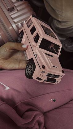 a pink toy car sitting on top of a bed next to a person's hand