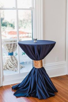 a table with a blue cloth draped over it in front of a window and wooden floor