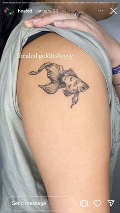 a woman's arm with a goldfish tattoo on the back of her shoulder