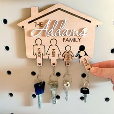 a person holding keys in front of a house shaped key holder that says, the addams family