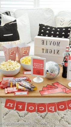 a movie night party with popcorn, drinks and snacks on a table in front of a couch