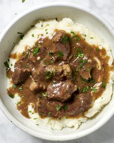 a white bowl filled with mashed potatoes topped with beef and gravy on top