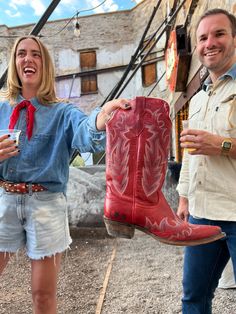 a man and woman standing next to each other with cowboy boots on their feet holding drinks