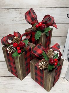 three christmas present boxes with pine cones, holly and red berries on them sitting on a white wooden surface