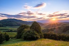 the sun is setting over some hills and trees