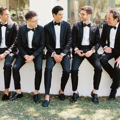 a group of men in tuxedos sitting next to each other on a wall