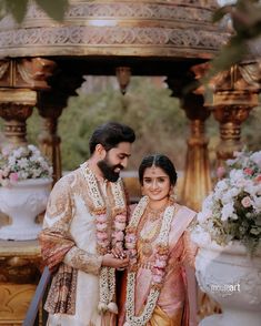 a man and woman standing next to each other in front of a gazebo with flowers