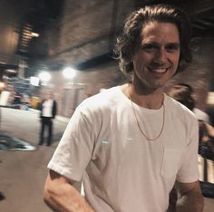 a man in white shirt holding a skateboard on street next to buildings and people