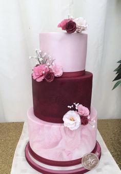 a three tiered cake with pink and purple frosting on the top, decorated with flowers