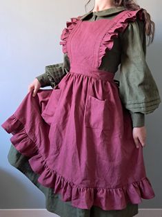 a woman wearing a dress with ruffles on the bottom and green sleeves, standing in front of a gray wall